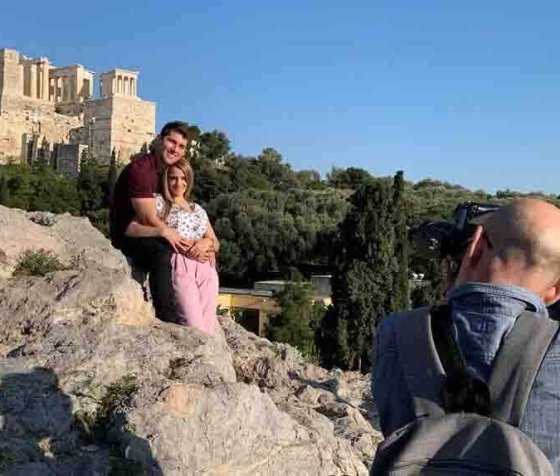 Professional portrait session at Areopagus hill of Athens. A young couple poses with panoramic views of Athens and Acropolis temple as a backdrop.